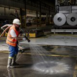 Deux employes de Novelis Sierre nettoient la boue entre les machines sur le site du fabriquant d'aluminium Novelis le jeudi 11 juillet 2024 a Sierre. Les entreprises Constellium et Novelis, devastees par le debordement du Rhone le week-end dernier, ont tenu jeudi une conférence de presse commune avec l'Etat du Valais. Ils reclament des mesures de protection urgentes. (KEYSTONE/Jean-Christophe Bott)